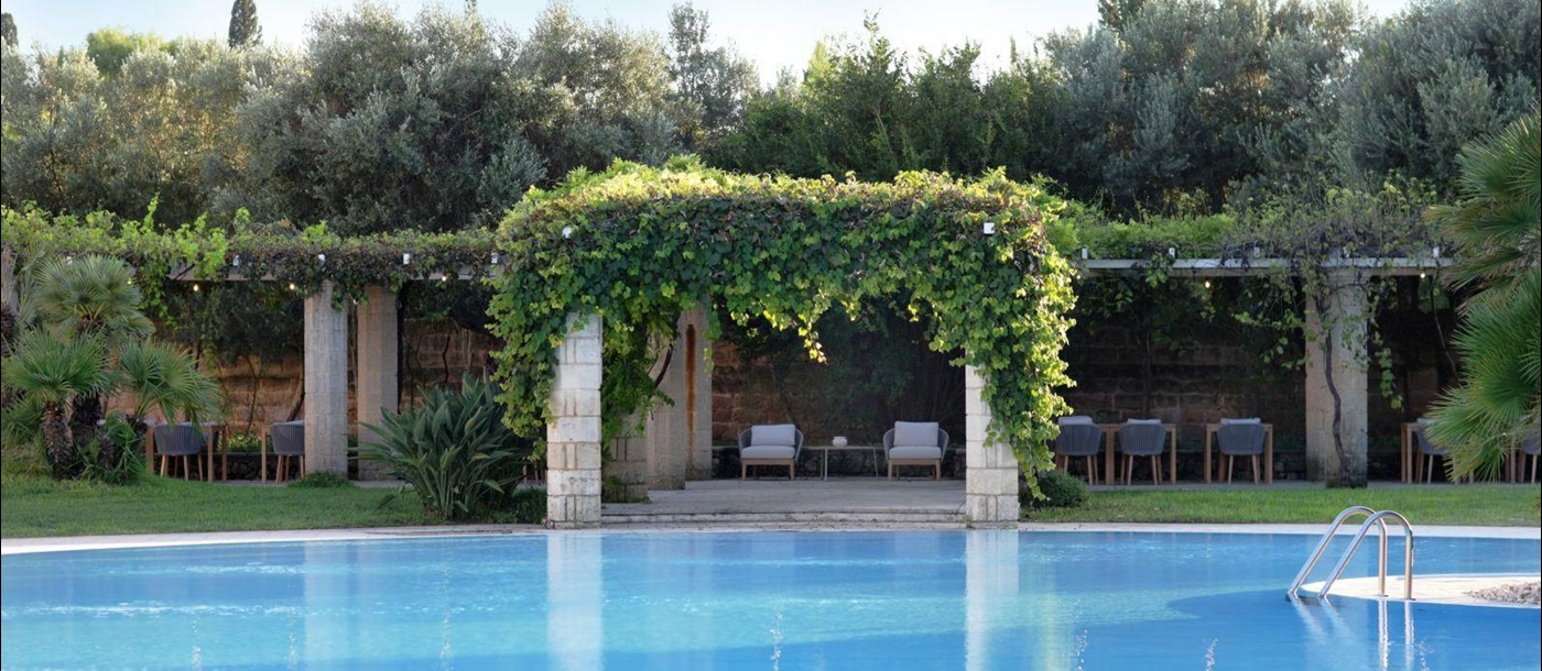 View over swimming pool to vine covered pergola at villa masseria dei papi in Puglian, Italy