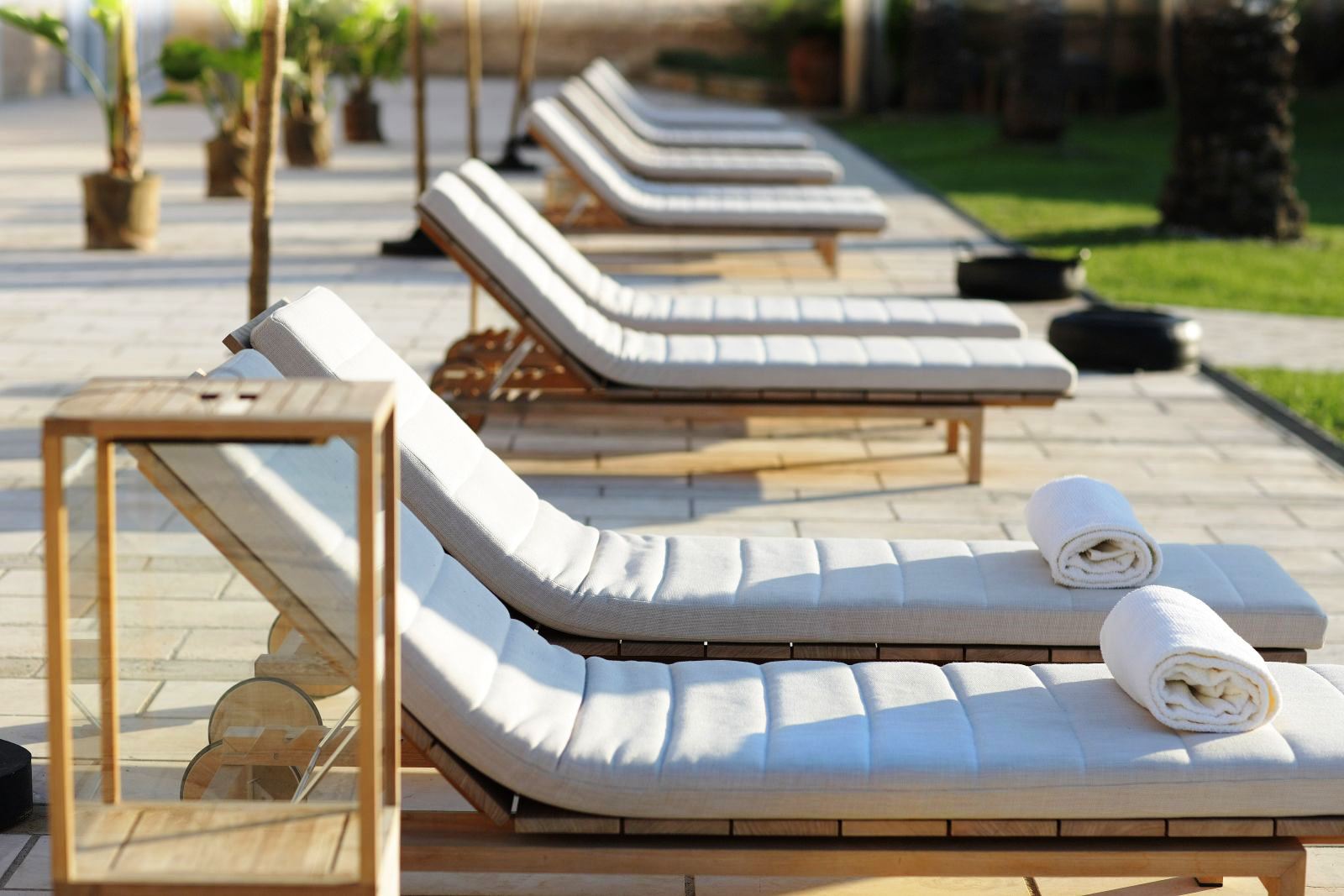 Row of 12 sunbeds with white cushions and rolled up towels on first two at villa masseria dei papi in Puglian, Italy