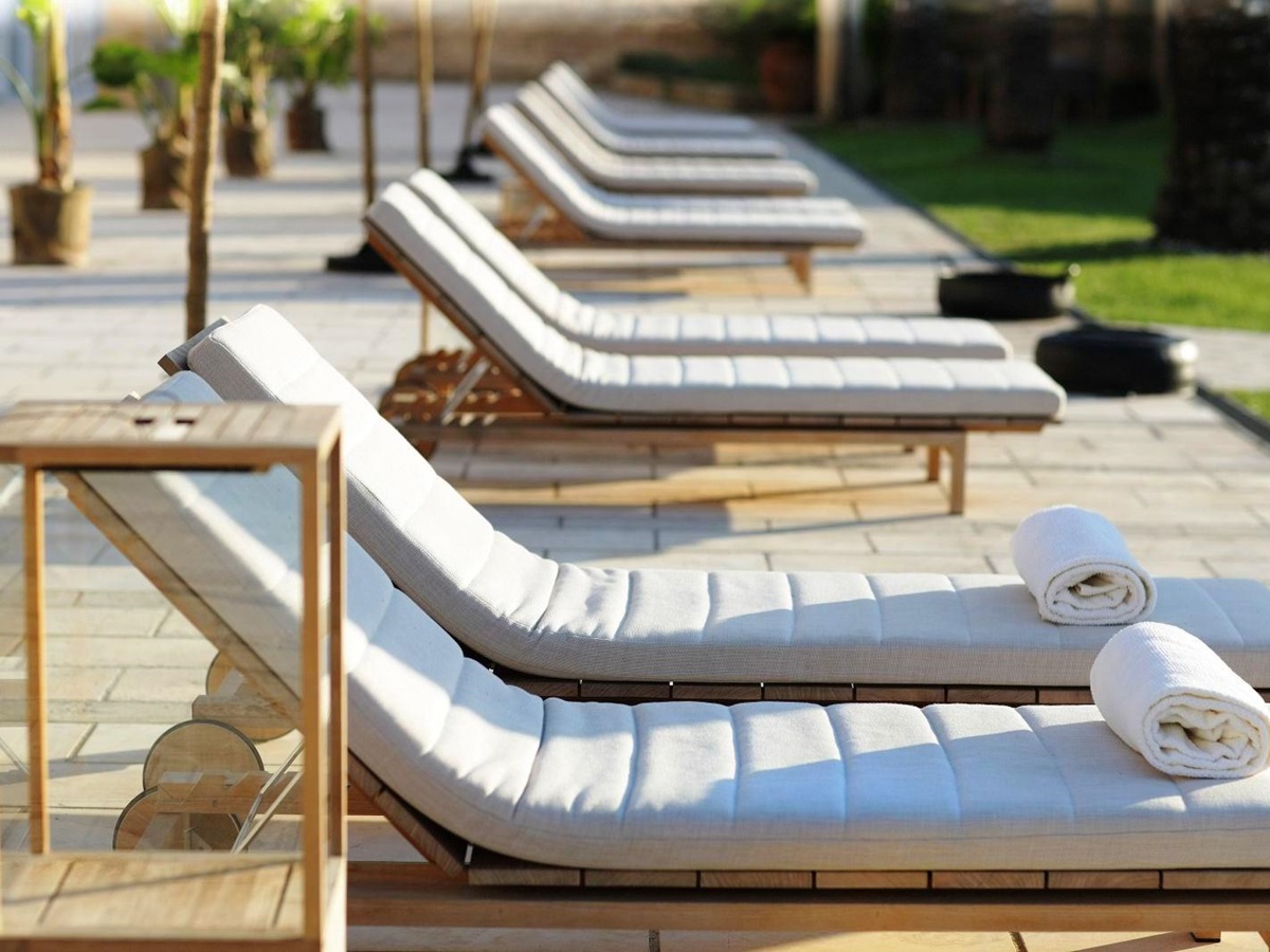 Row of 12 sunbeds with white cushions and rolled up towels on first two at villa masseria dei papi in Puglian, Italy