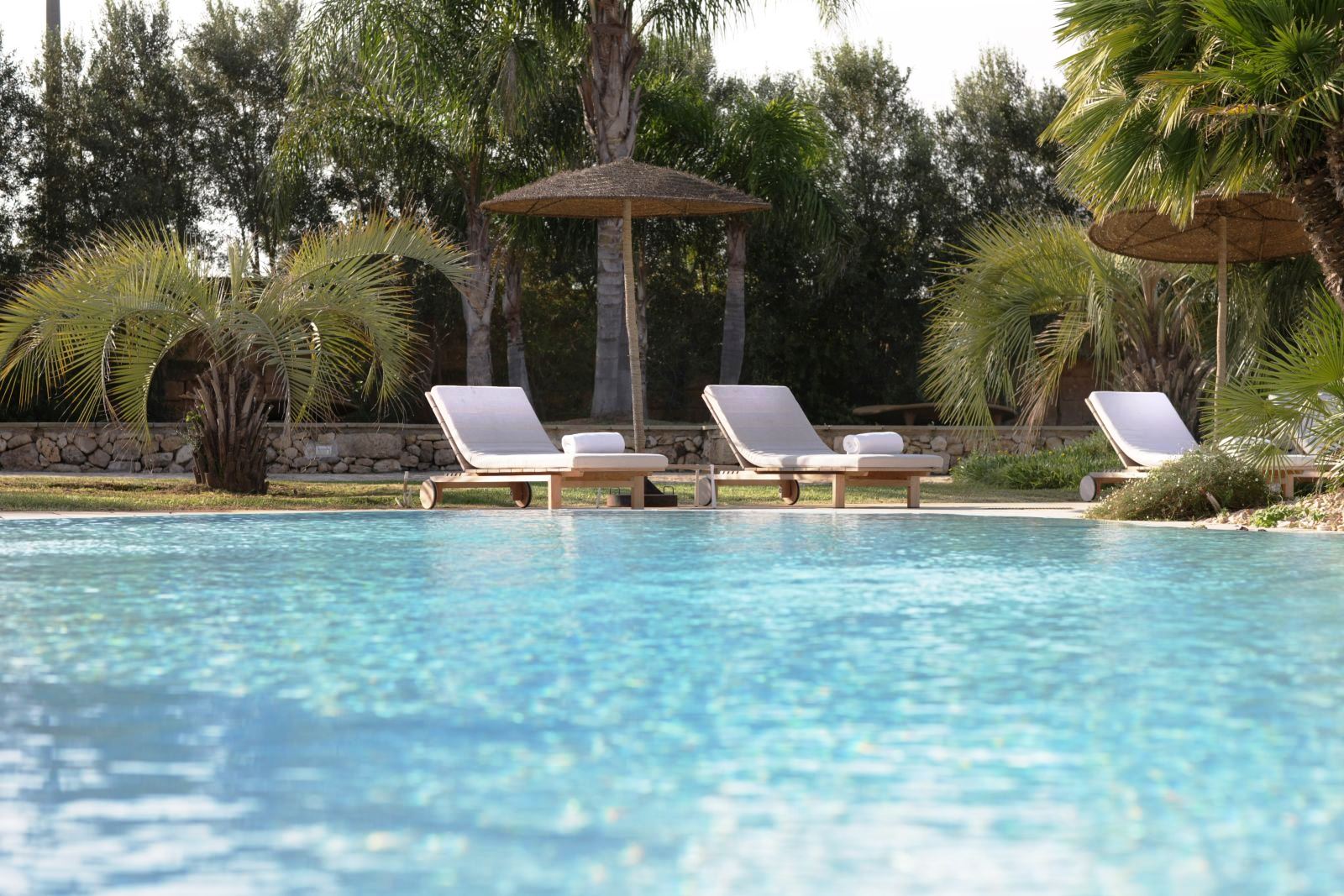 Three white sunbeds under wicker sun umbrellas by side of pool at villa masseria dei papi in Puglian, Italy