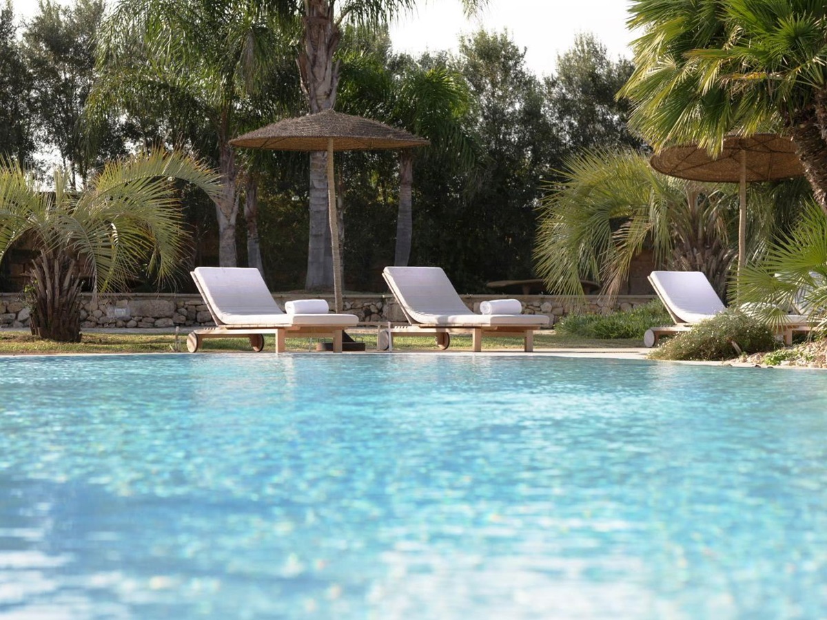 Three white sunbeds under wicker sun umbrellas by side of pool at villa masseria dei papi in Puglian, Italy