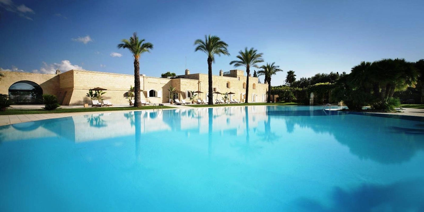 view over the pool of the exterior of villa masseria dei papi in Puglia, Italy with a line of 4 palm trees in front