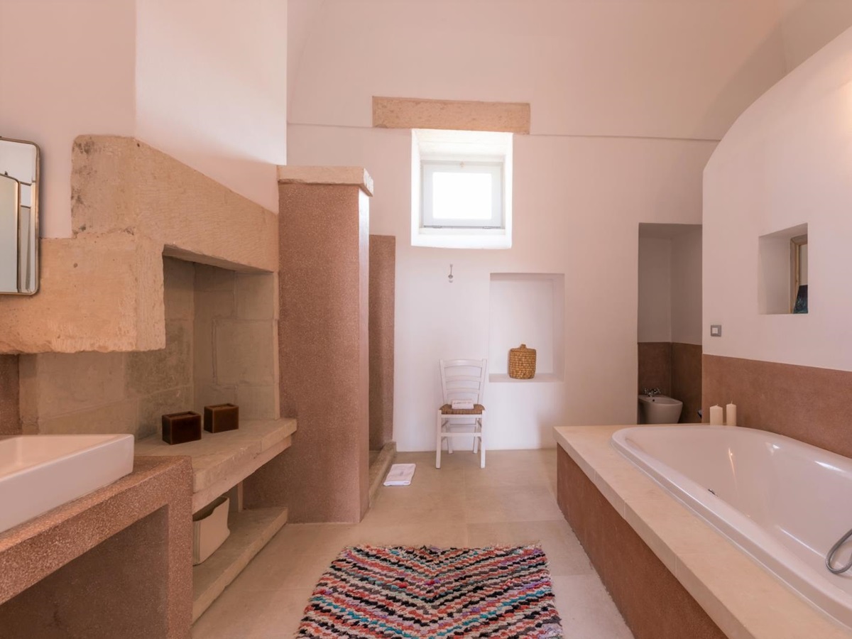 Bathroom with bath, sink, patterned rug, chair and small window at Palazzo del Duca in Puglia, Italy