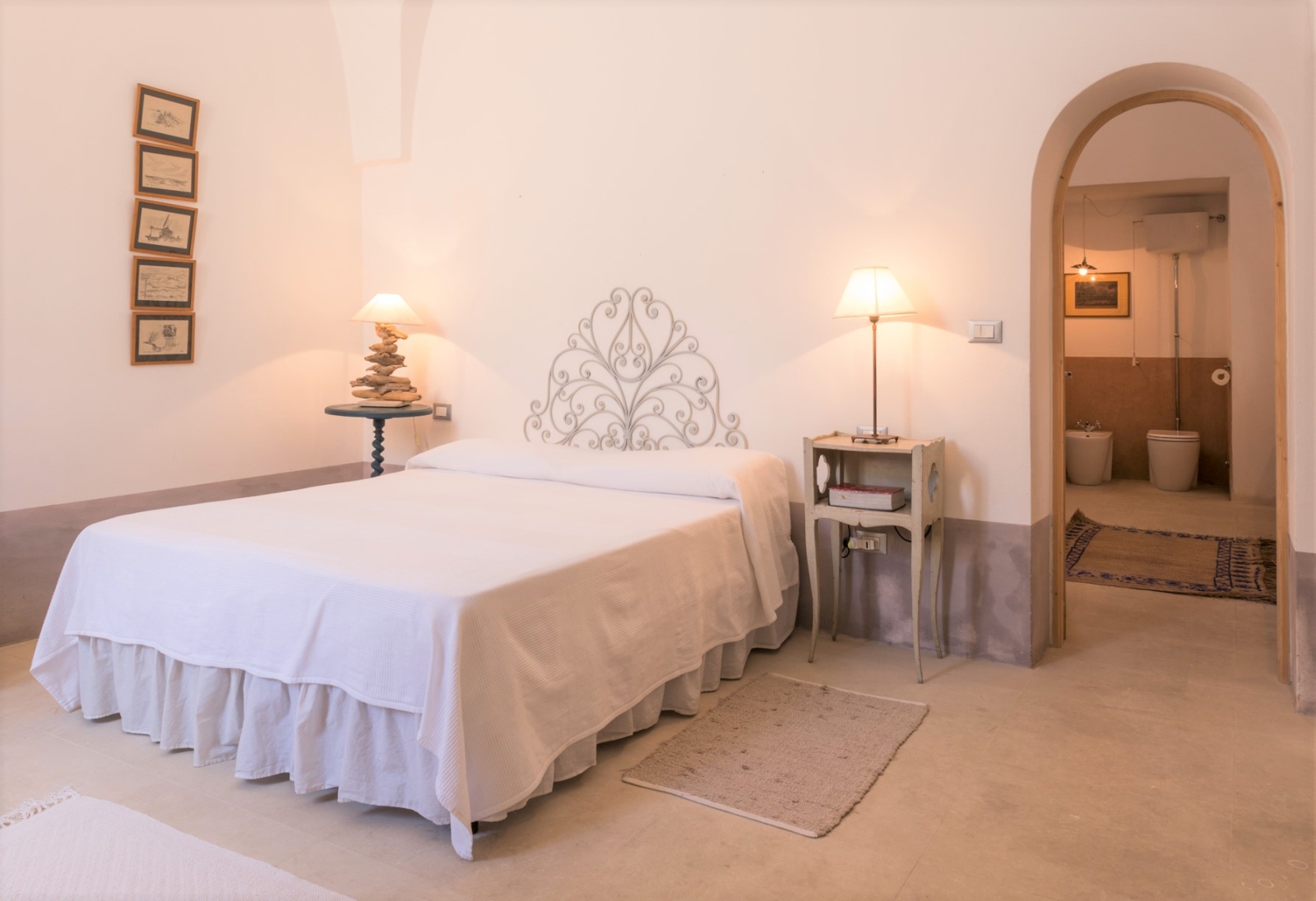 Bedroom with double bed, bedside tables, lamps, picture frames and ensuite bathroom at Palazzo del Duca in Puglia, Italy