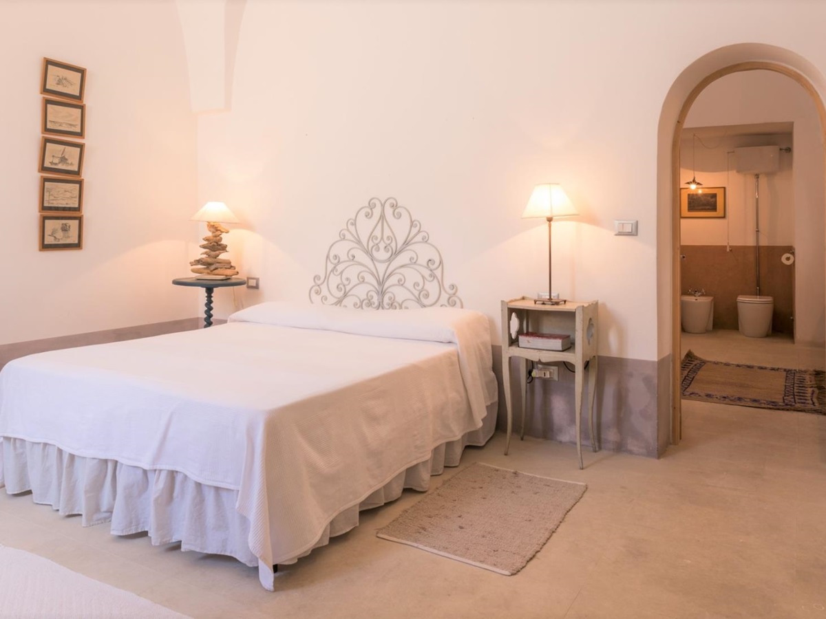 Bedroom with double bed, bedside tables, lamps, picture frames and ensuite bathroom at Palazzo del Duca in Puglia, Italy