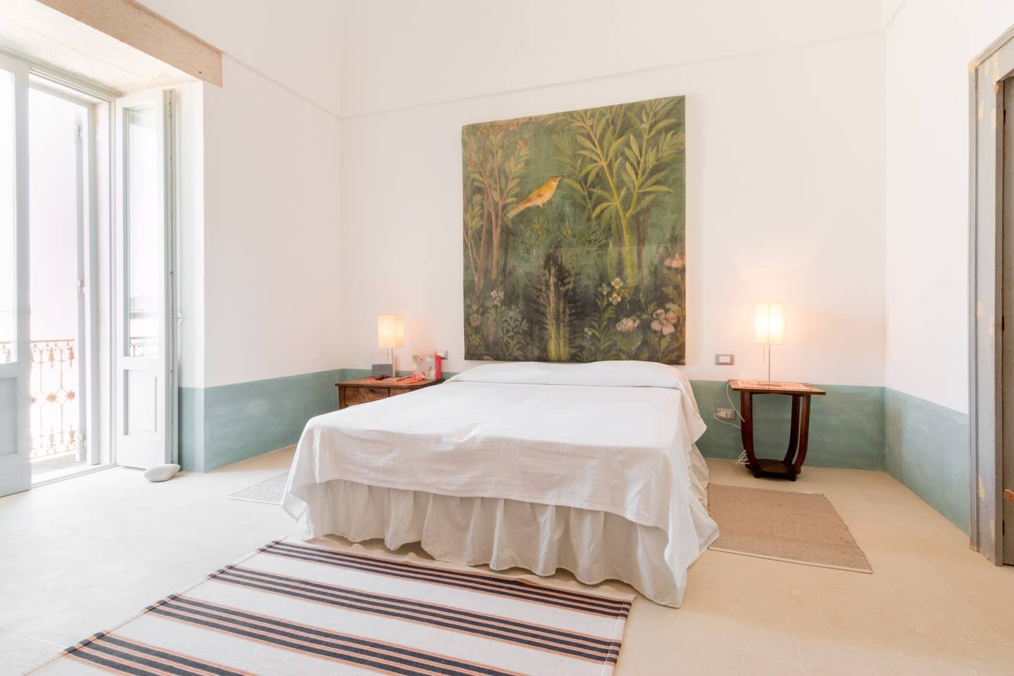 Bedroom with double bed, bedside tables, lamps, large painting, rug and balcony at Palazzo del Duca in Puglia, Italy