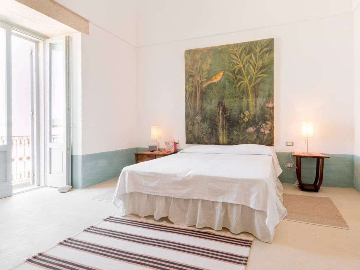 Bedroom with double bed, bedside tables, lamps, large painting, rug and balcony at Palazzo del Duca in Puglia, Italy