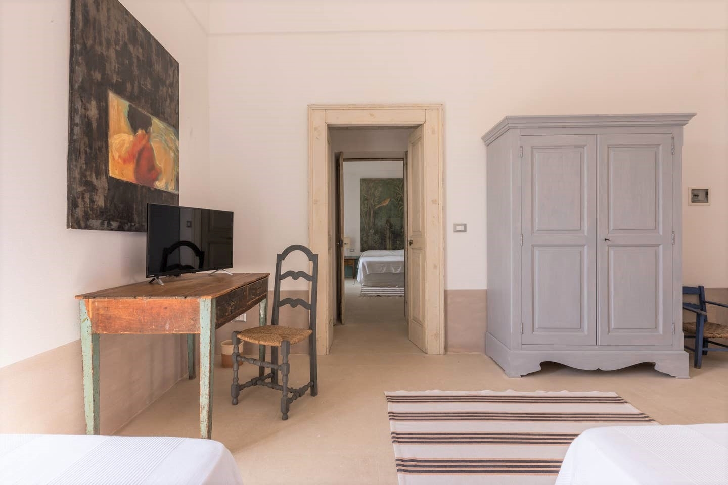 Bedroom with twin beds, desk, chair, painting, TV and wardrobe at Palazzo del Duca in Puglia, Italy
