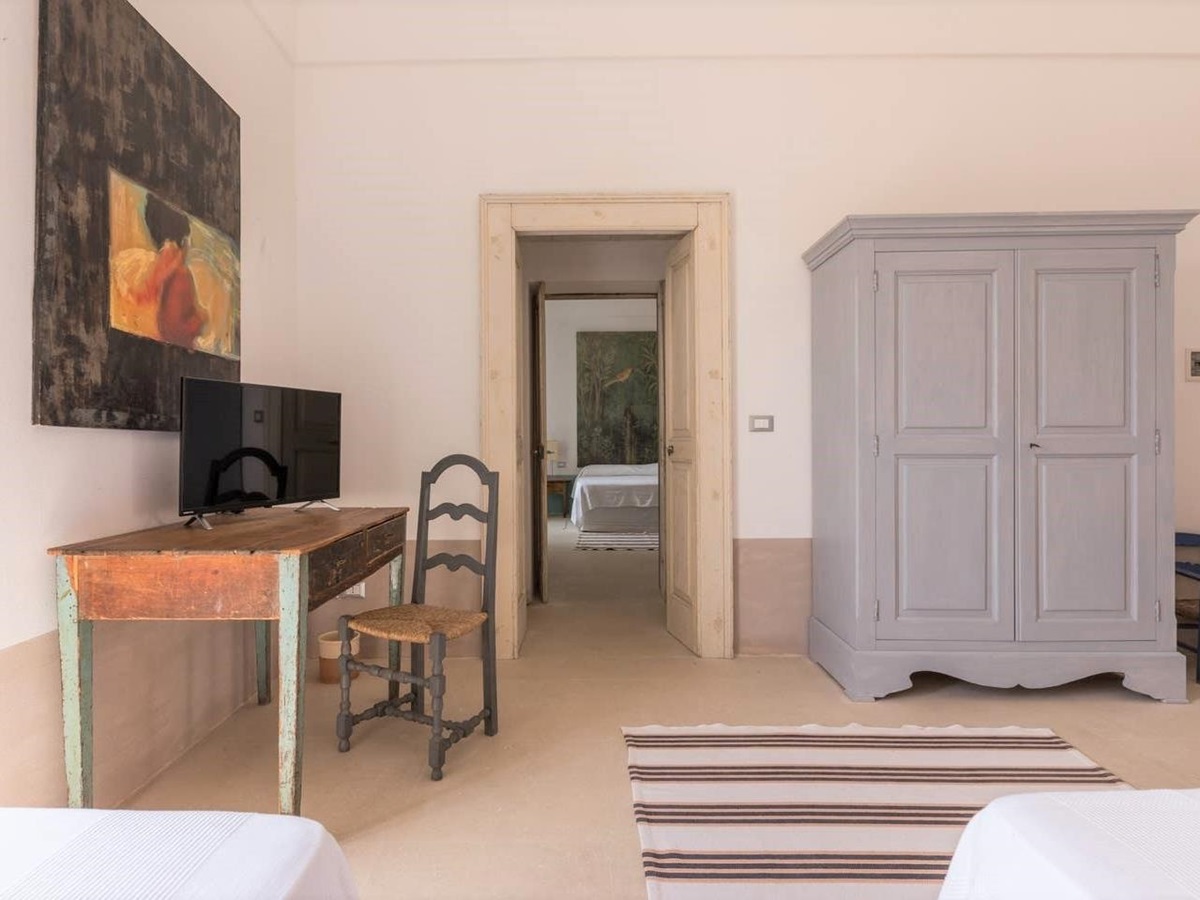 Bedroom with twin beds, desk, chair, painting, TV and wardrobe at Palazzo del Duca in Puglia, Italy