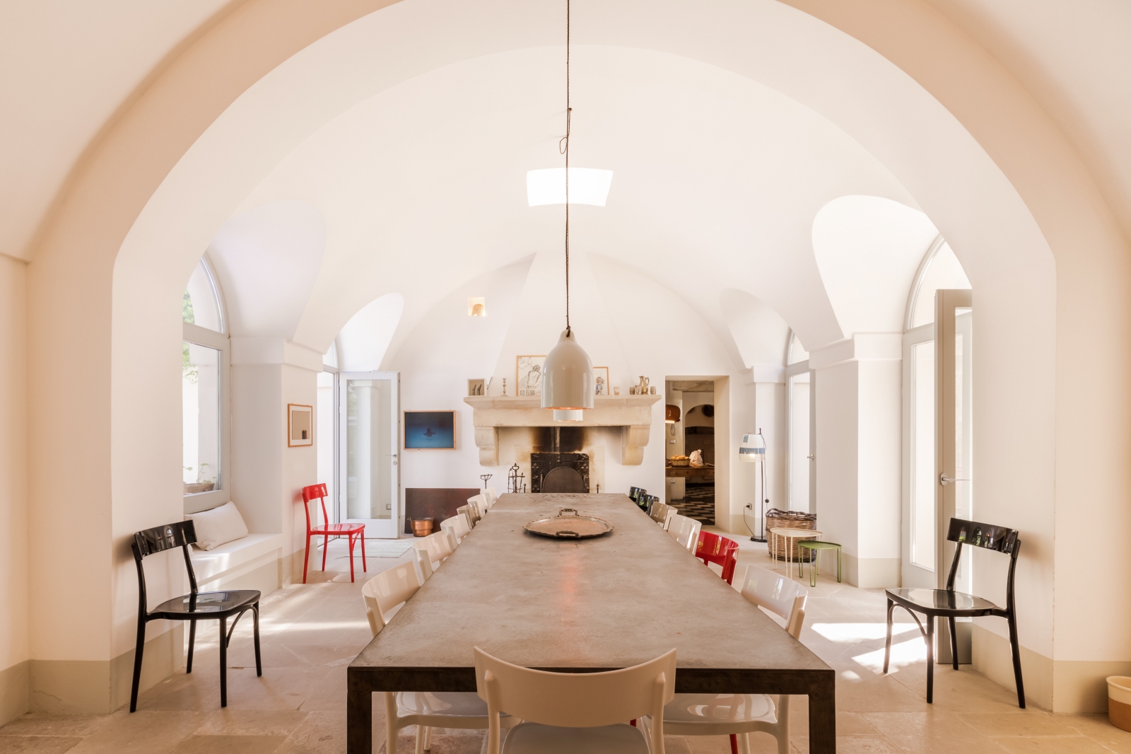 Dining room with long table, 16 chairs, hanging light, fireplace and French doors at Palazzo del Duca in Puglia, Italy