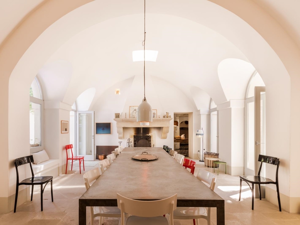 Dining room with long table, 16 chairs, hanging light, fireplace and French doors at Palazzo del Duca in Puglia, Italy