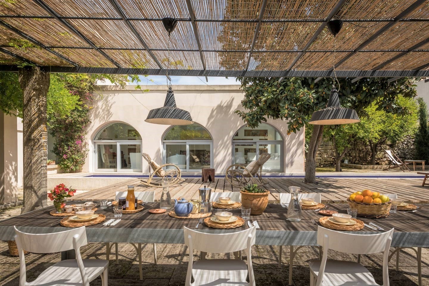 Covered outdoor dining area with table, chairs, fresh food and drink & hanging lights at Palazzo del Duca in Puglia, Italy