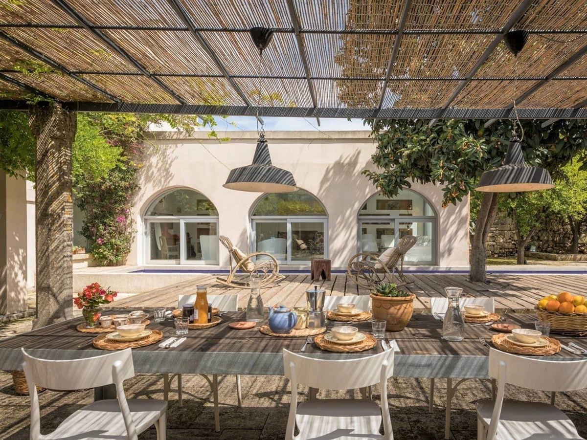 Covered outdoor dining area with table, chairs, fresh food and drink & hanging lights at Palazzo del Duca in Puglia, Italy