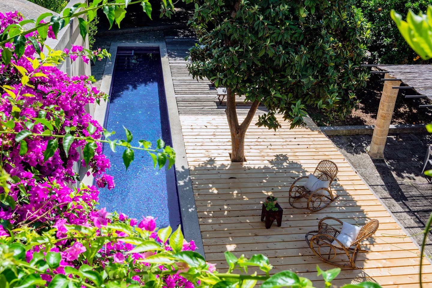 Long swimming pool and decking area with flowers, tree and rocking chairs at Palazzo del Duca in Puglia, Italy