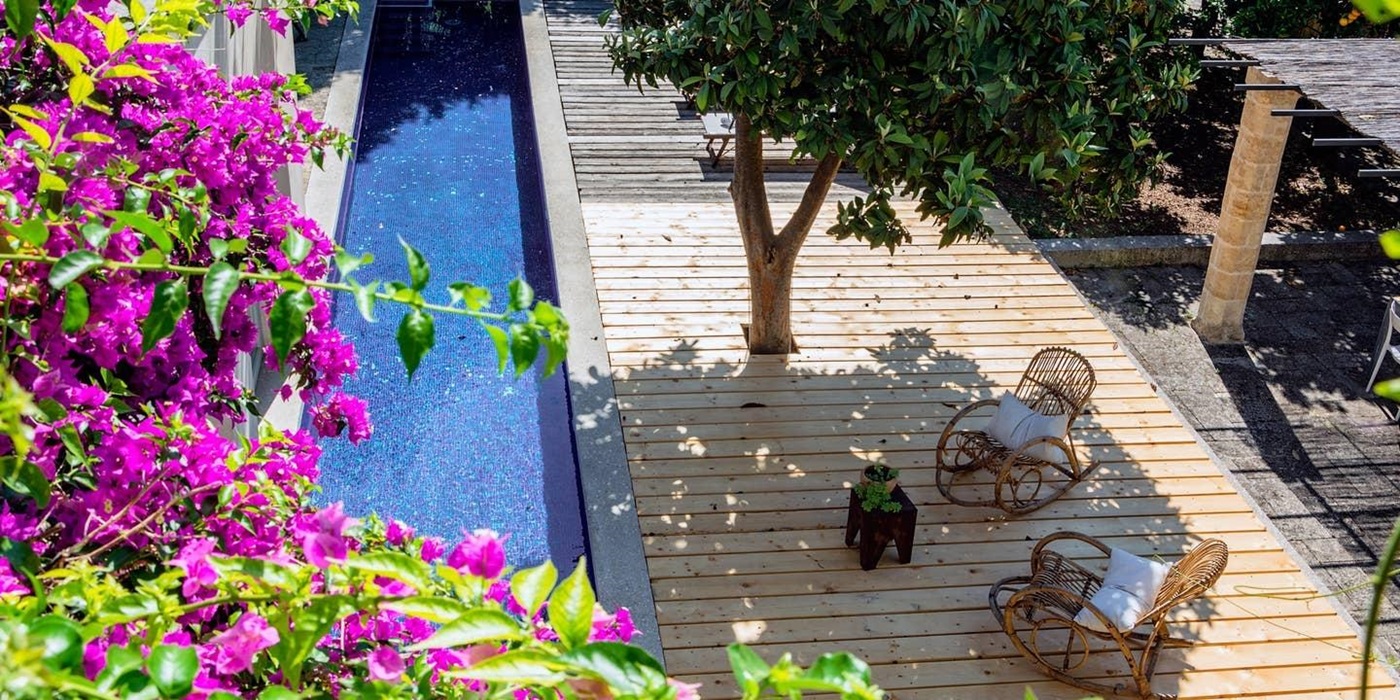 Long swimming pool and decking area with flowers, tree and rocking chairs at Palazzo del Duca in Puglia, Italy