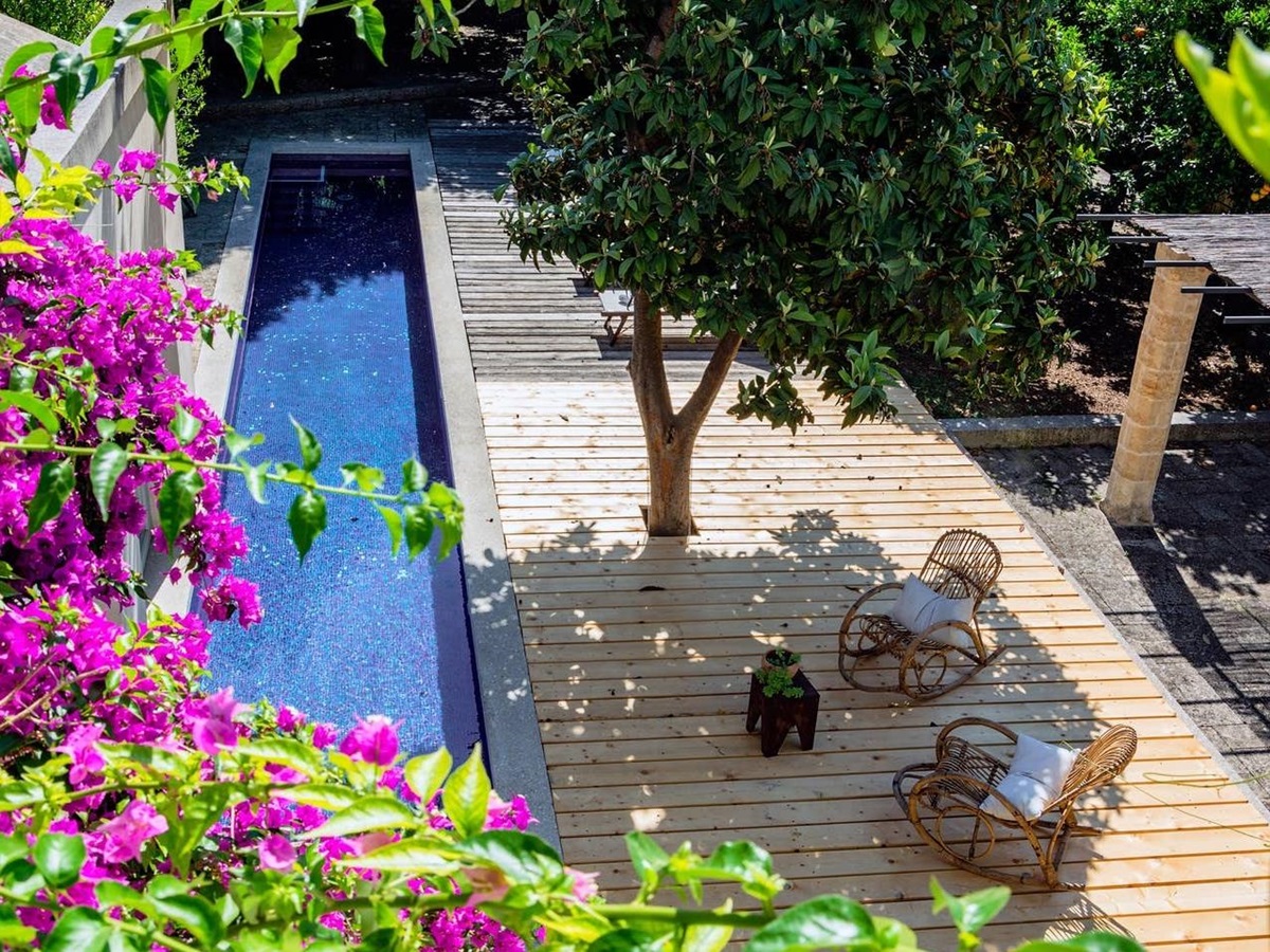 Long swimming pool and decking area with flowers, tree and rocking chairs at Palazzo del Duca in Puglia, Italy