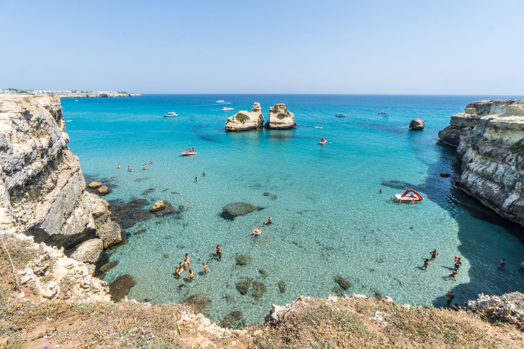 Visitors of Torre dell'Orso beach swimming in the sea near its distinct rock formation