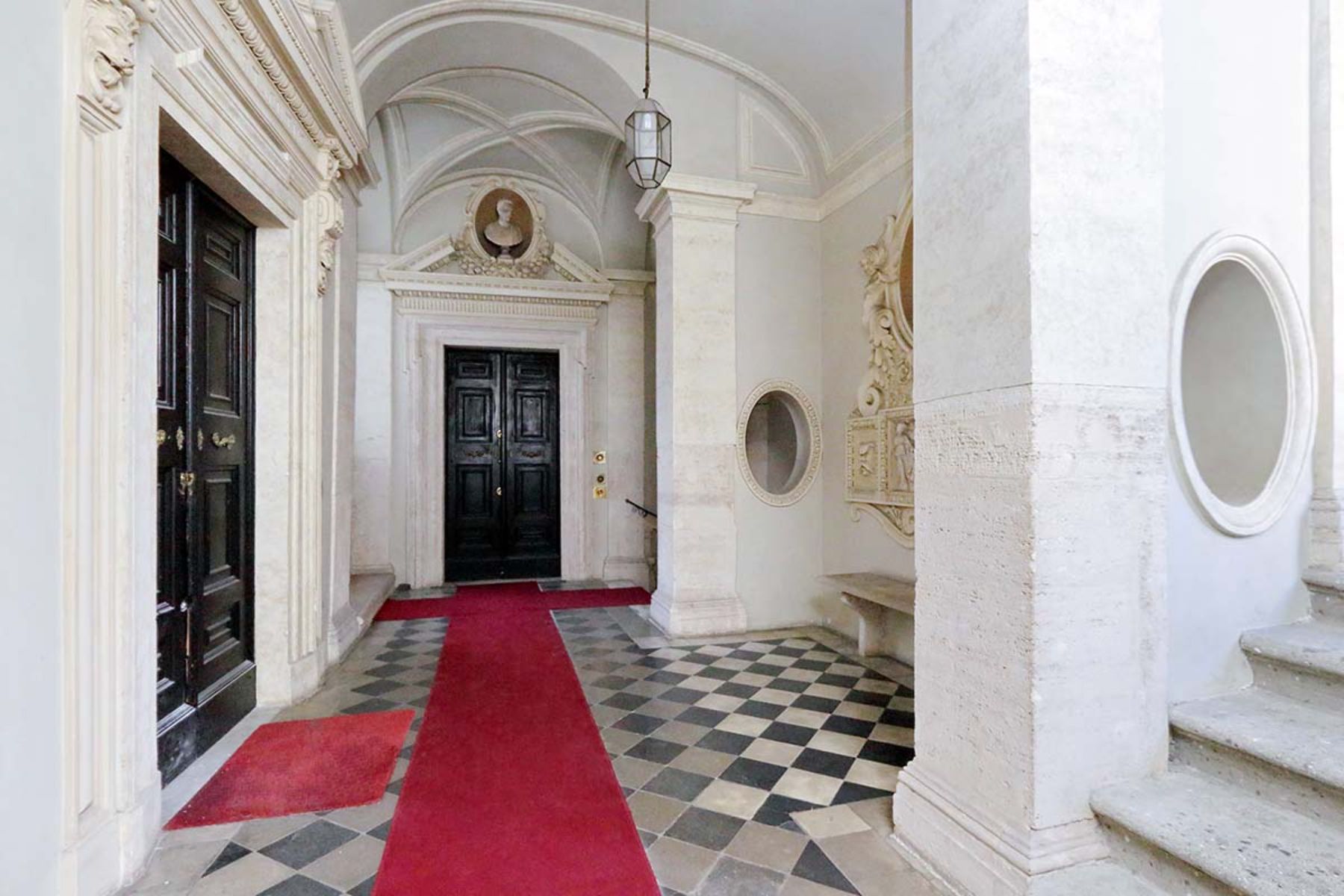 View of the entrance lobby at the Costaguti Apartment in Rome featuring marble floors and large black doors