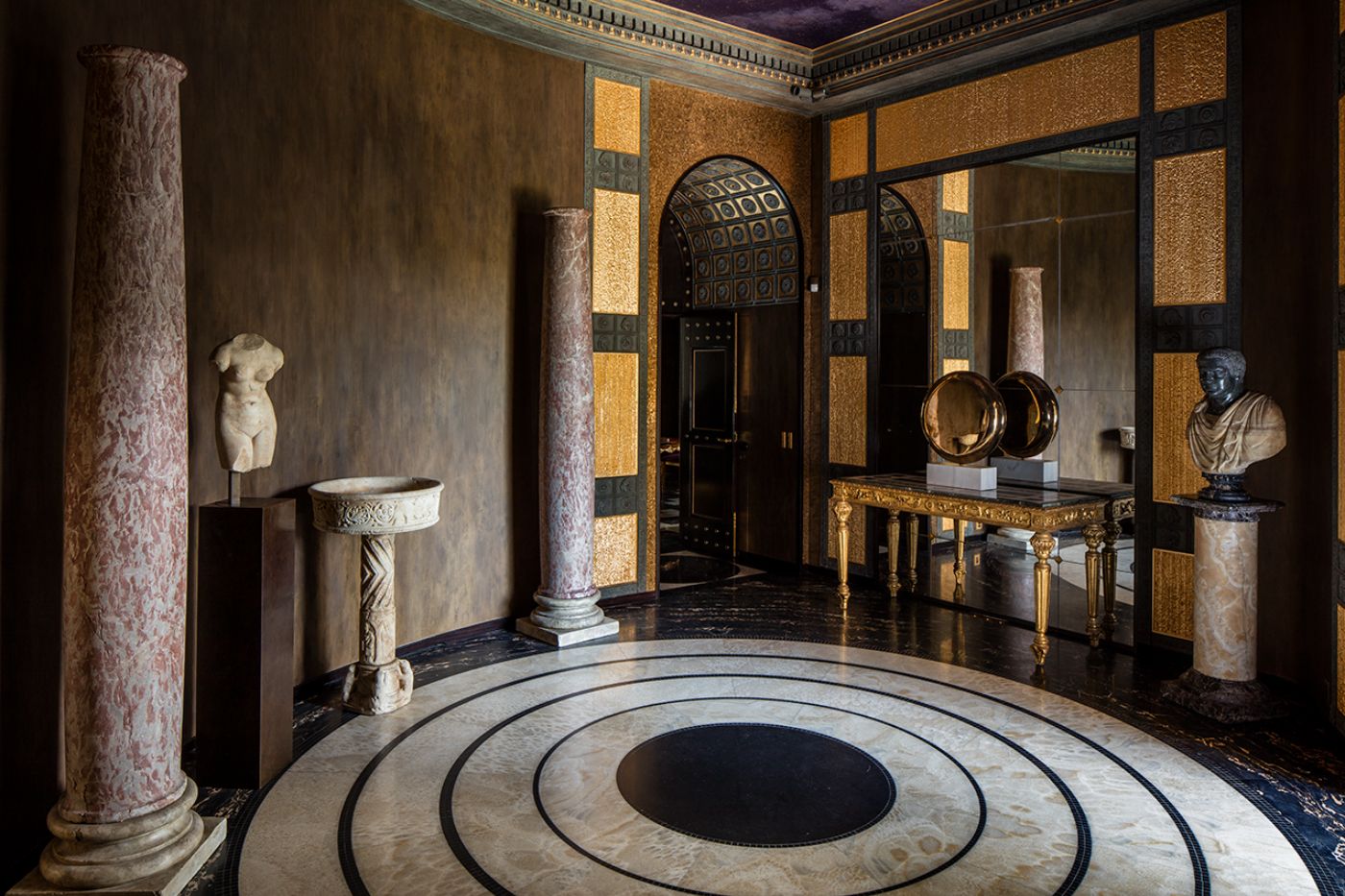 A large circular corridor space adorned with Italian themed sculptures and columns at Villa Clara.