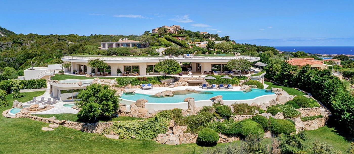 Large villa with pools and gardens in the foreground and sea on the horizon at The Rock in Sardinia