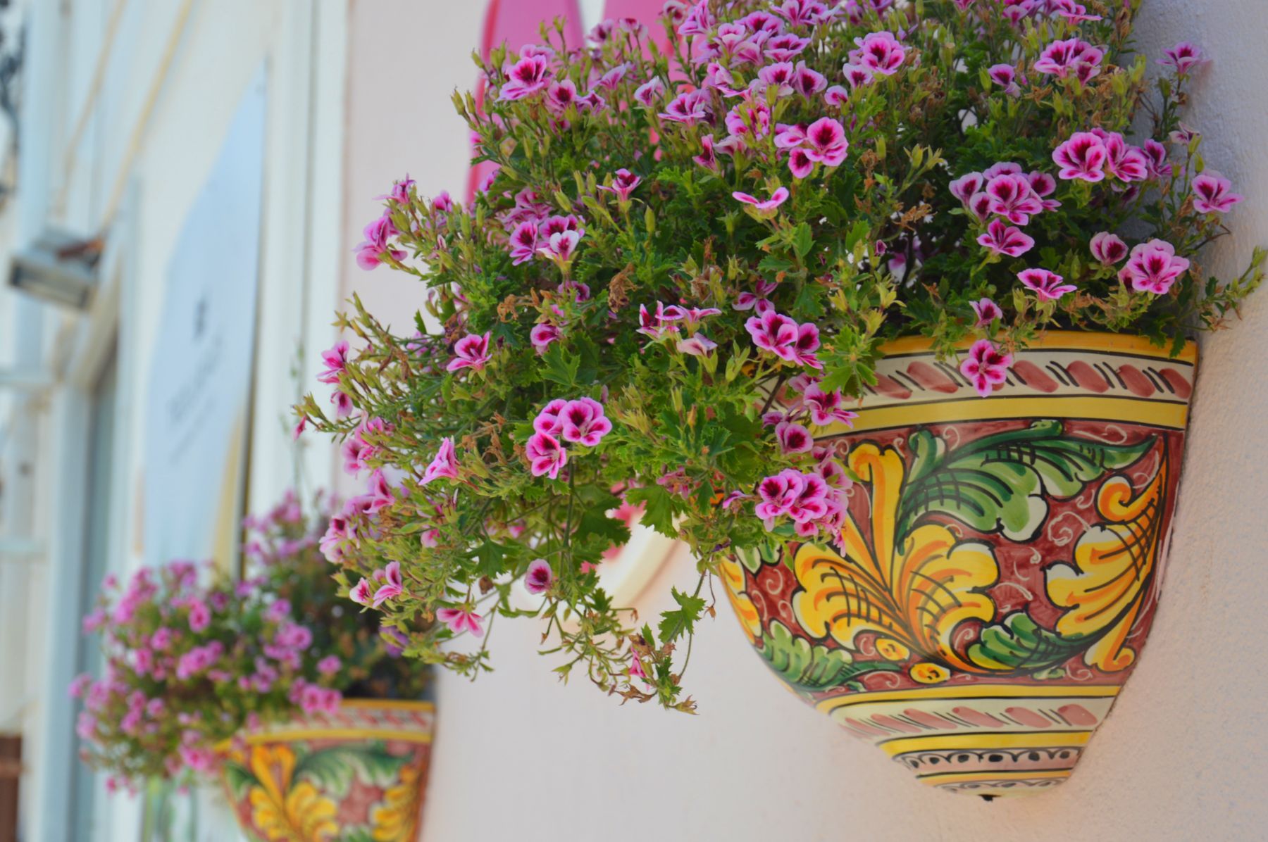 Purple flowers in a painted ceramic vase hanging on the wall in Sicily
