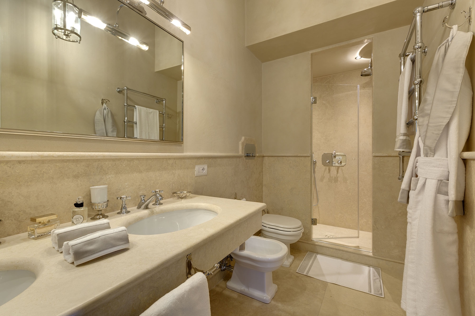 Bathroom with sinks, mirror, toilet, bidet, shower, robe, towel rail & toiletries at Castel Botticelli in Tuscany, Italy