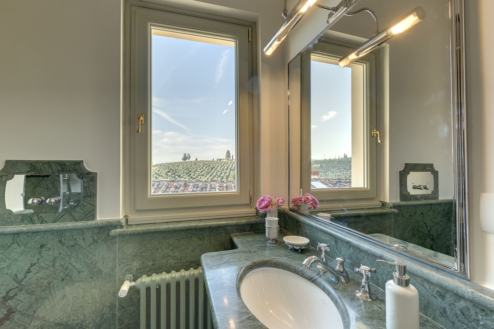 Bathroom with blue marble decoration, sink, flowers, window, large mirror and radiator at Castel Botticelli in Tuscany, Italy