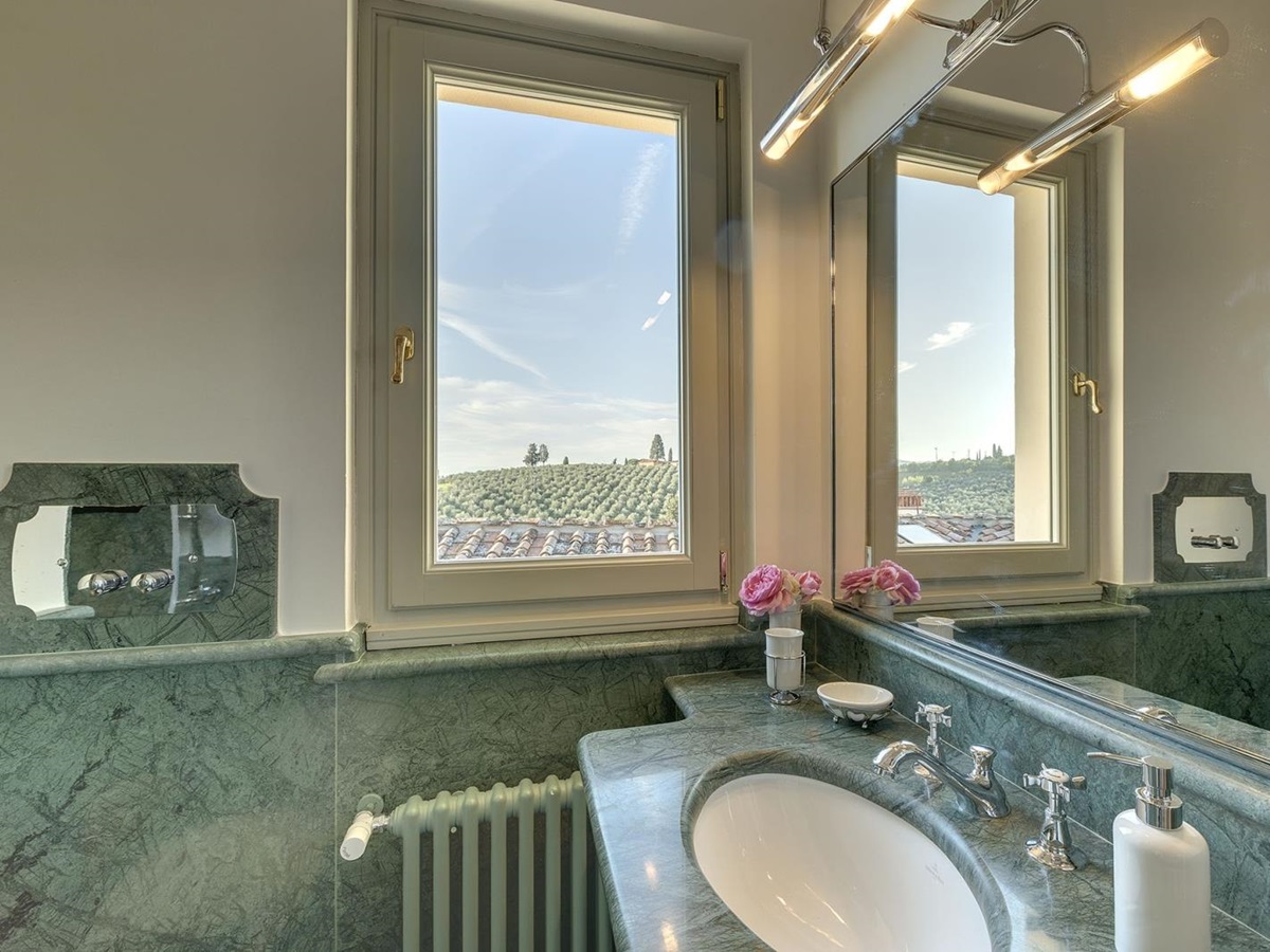 Bathroom with blue marble decoration, sink, flowers, window, large mirror and radiator at Castel Botticelli in Tuscany, Italy