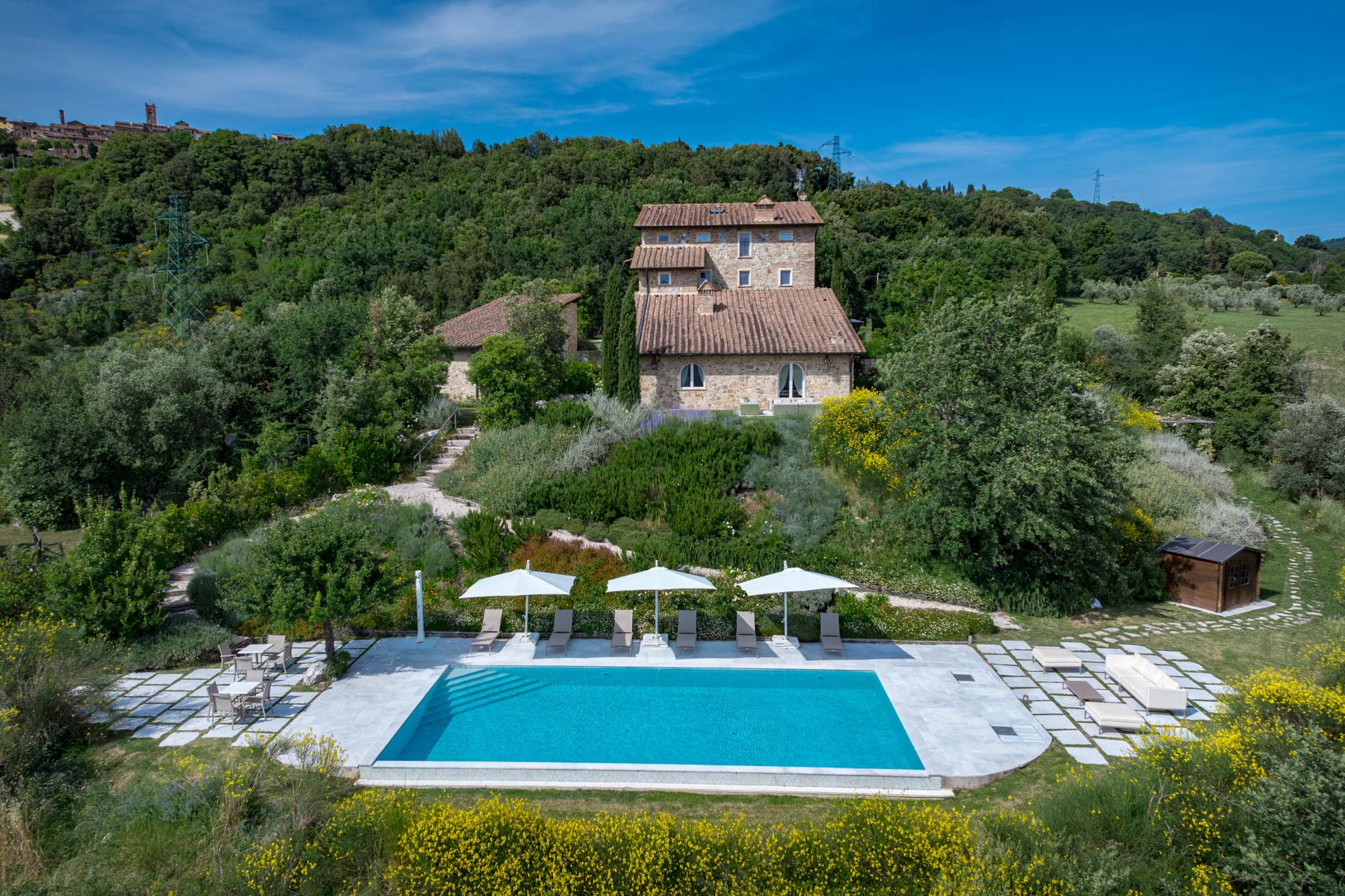 View of the outdoor pool surrounded by trees with view of Villa Il Mugnello behind the pool in Tuscany