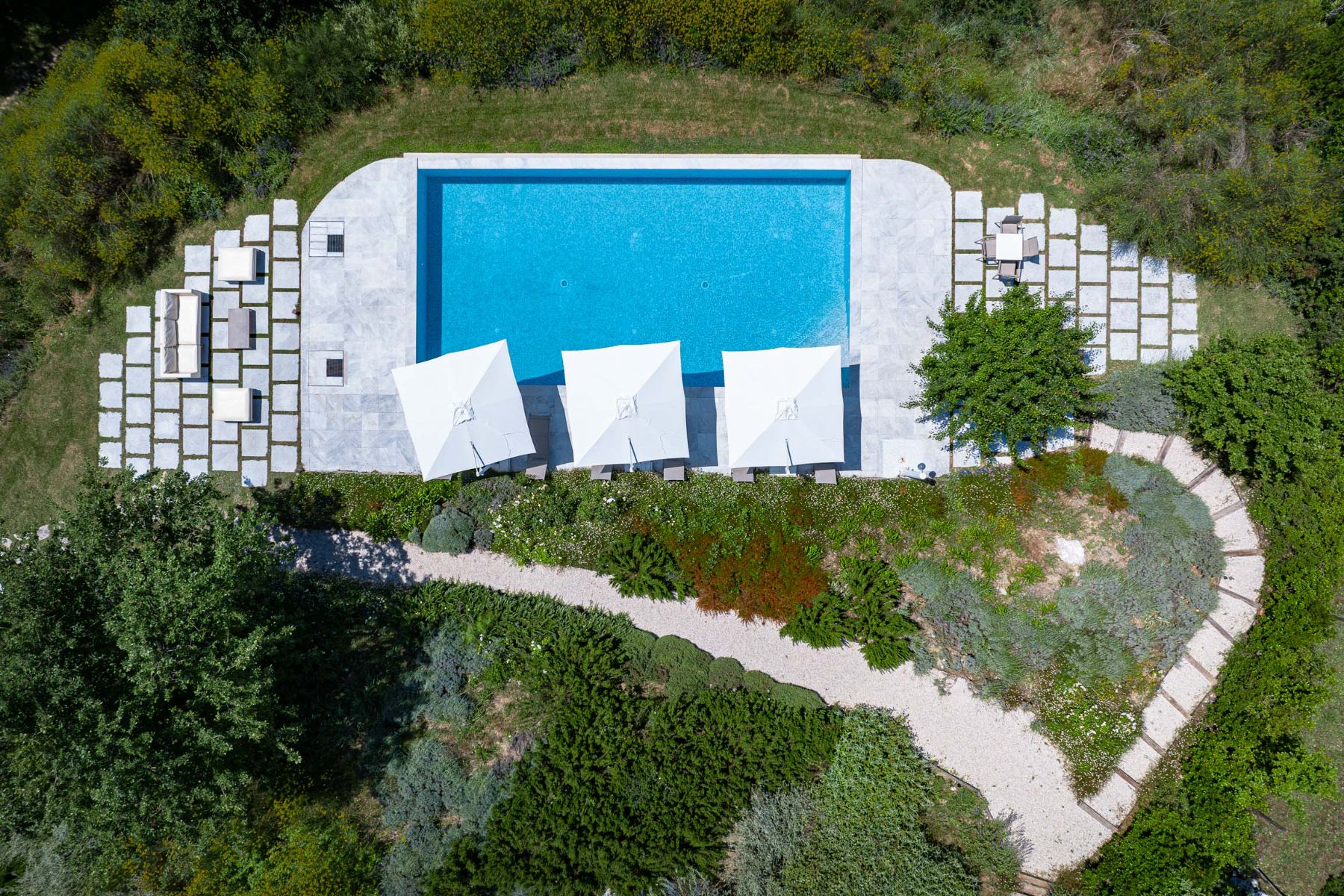 Drone view of the outdoor pool featuring white umbrellas at Villa Il Mugnello in Tuscany