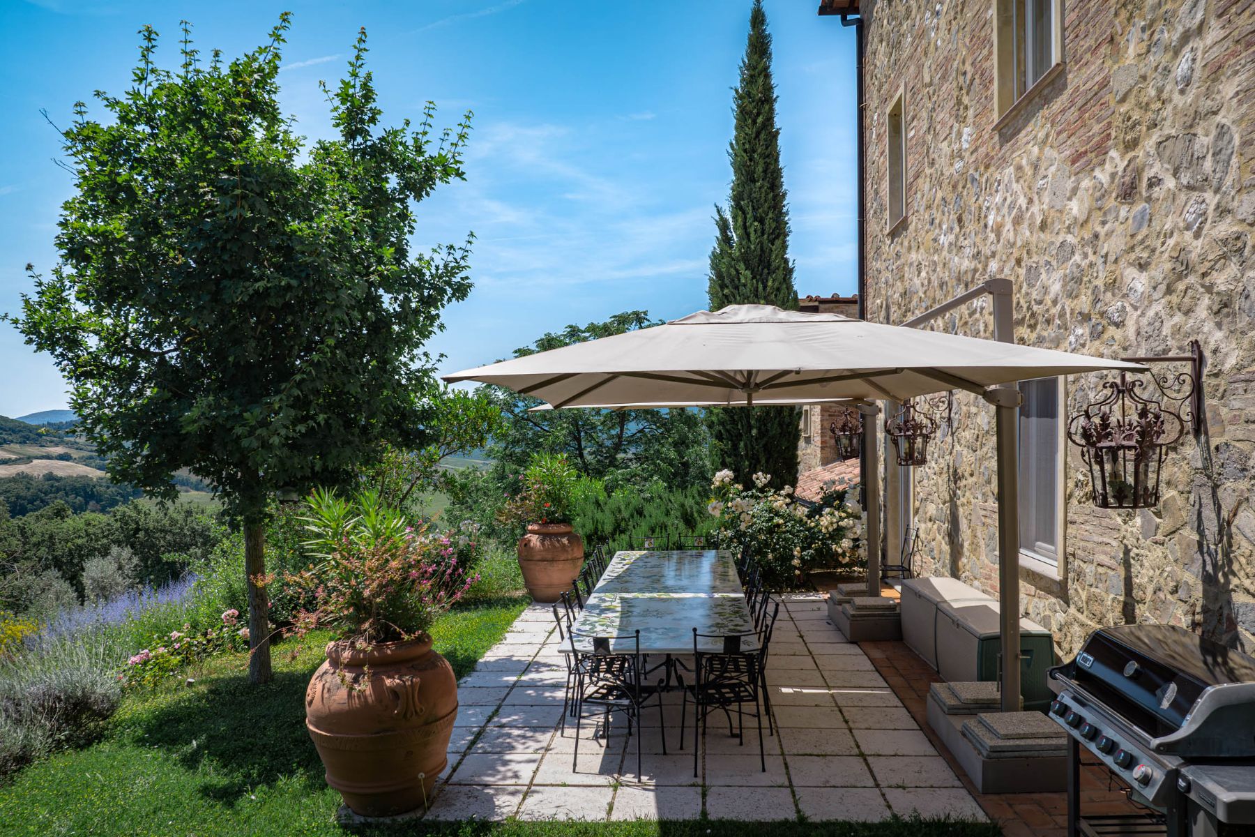 Outdoor dining area with large table and view of the gardens and Tuscan hills at Villa Il Mugnello