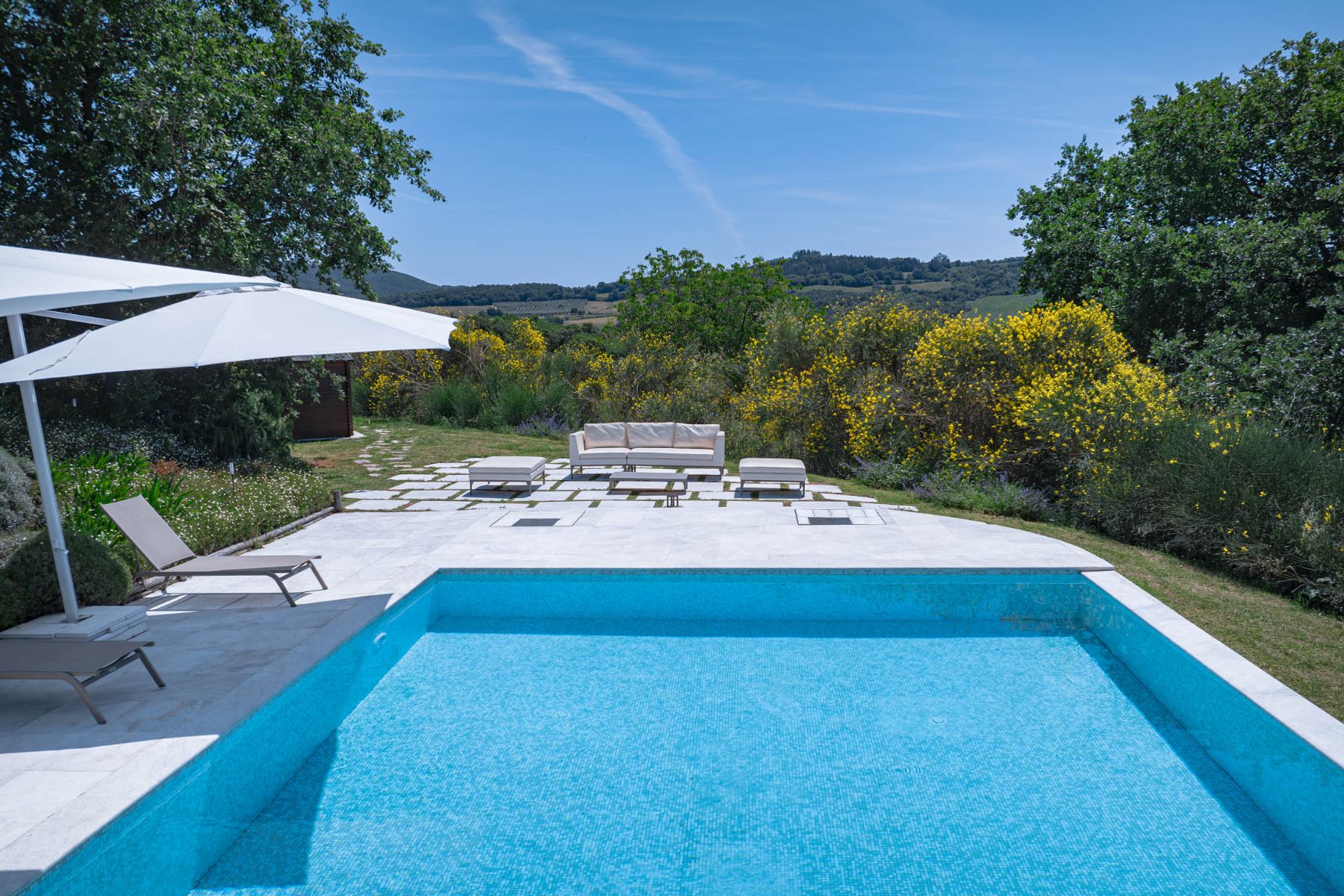Up close view of the oudoor pool at Villa Il Mugnello in Tuscny with view of white sun loungers and umbrellas