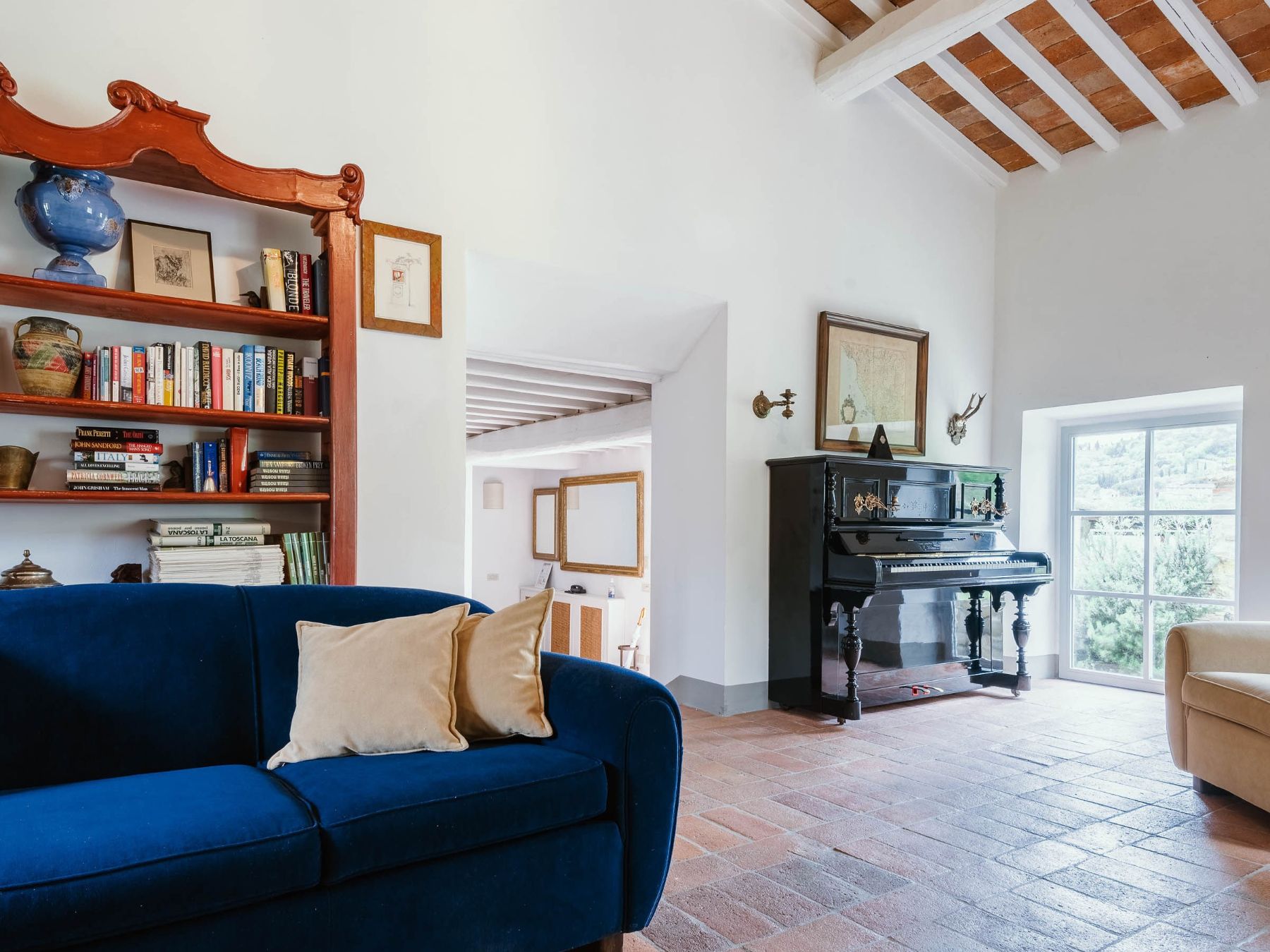 Cottage living room with grand piano and wooden bookshelf at Il Prato di Vignamaggio in Tuscany