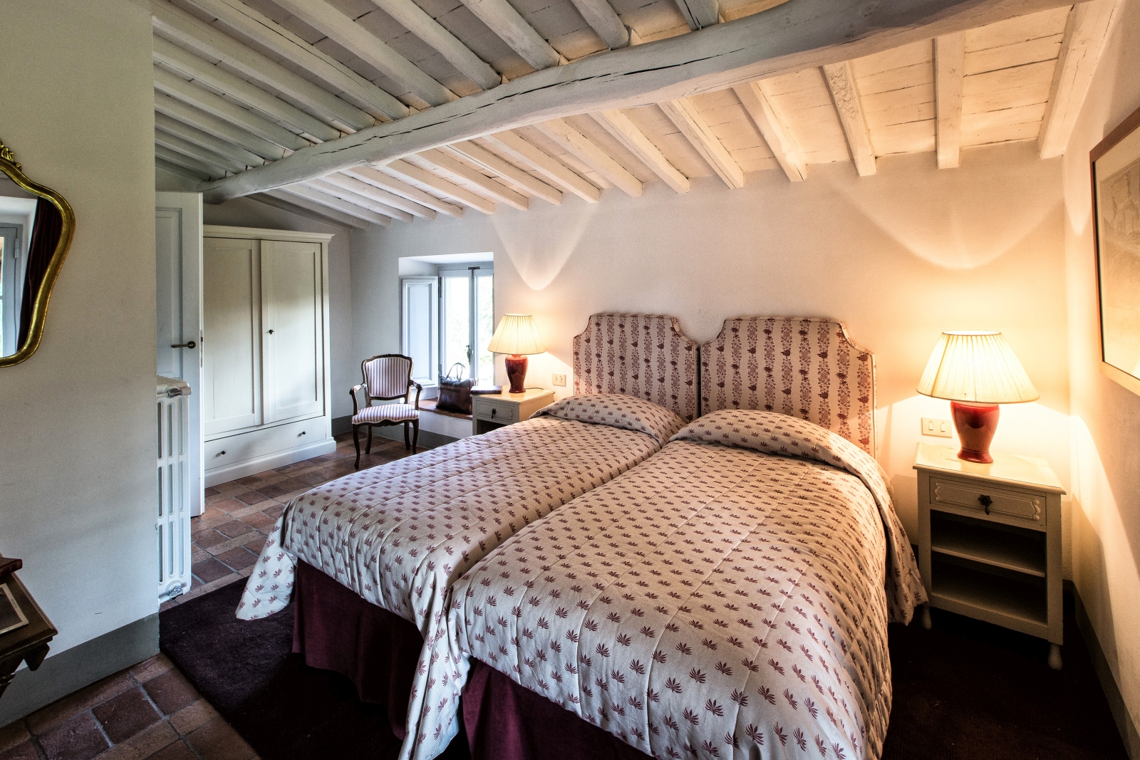 Bedroom with twin beds, bedside tables, lamps, chair, wardrobe and mirror at Il Prato di Vignamaggio in Tuscany, Italy