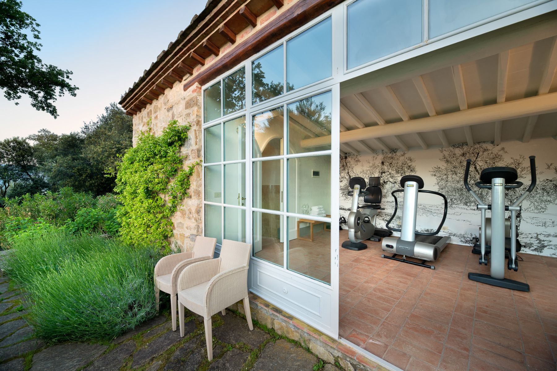 Gym building with different machines and two chairs outside the building at Il Prato di Vignamaggio in Tuscany