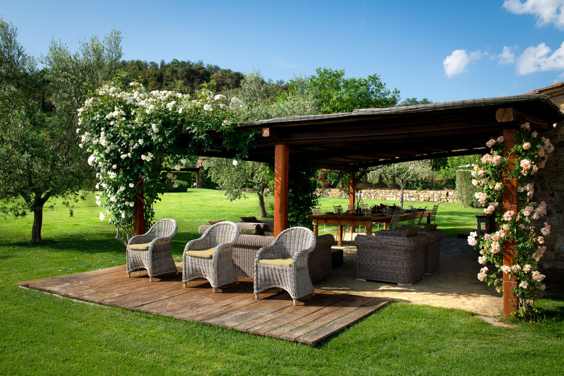 Outdoor dining area with a sheltered roof and armchairs in the garden at Il Prato di Vignammagio in Tuscany