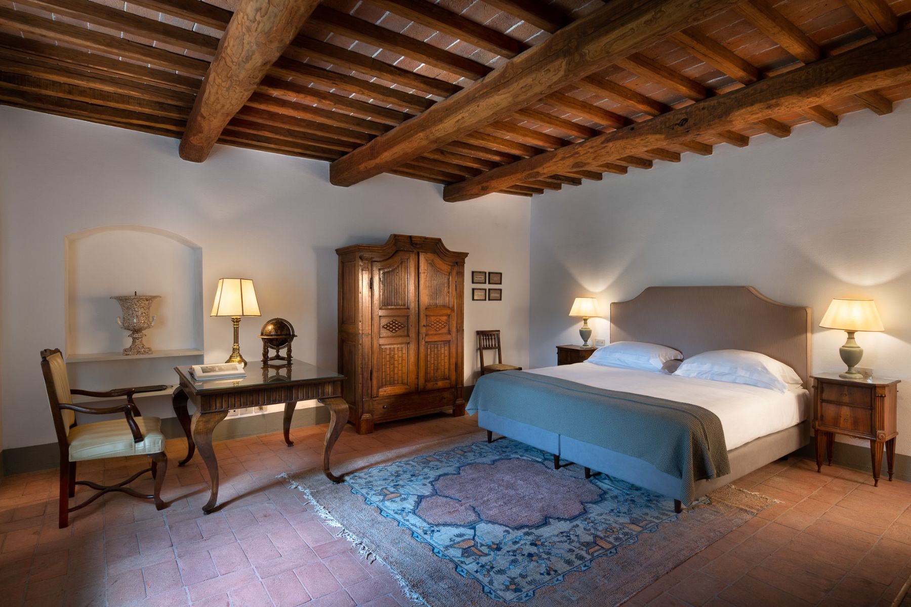 Bedroom with large double bed and a wooden table and armchair and wooden ceiling beams at il Prato di Vignammagio in Tuscany