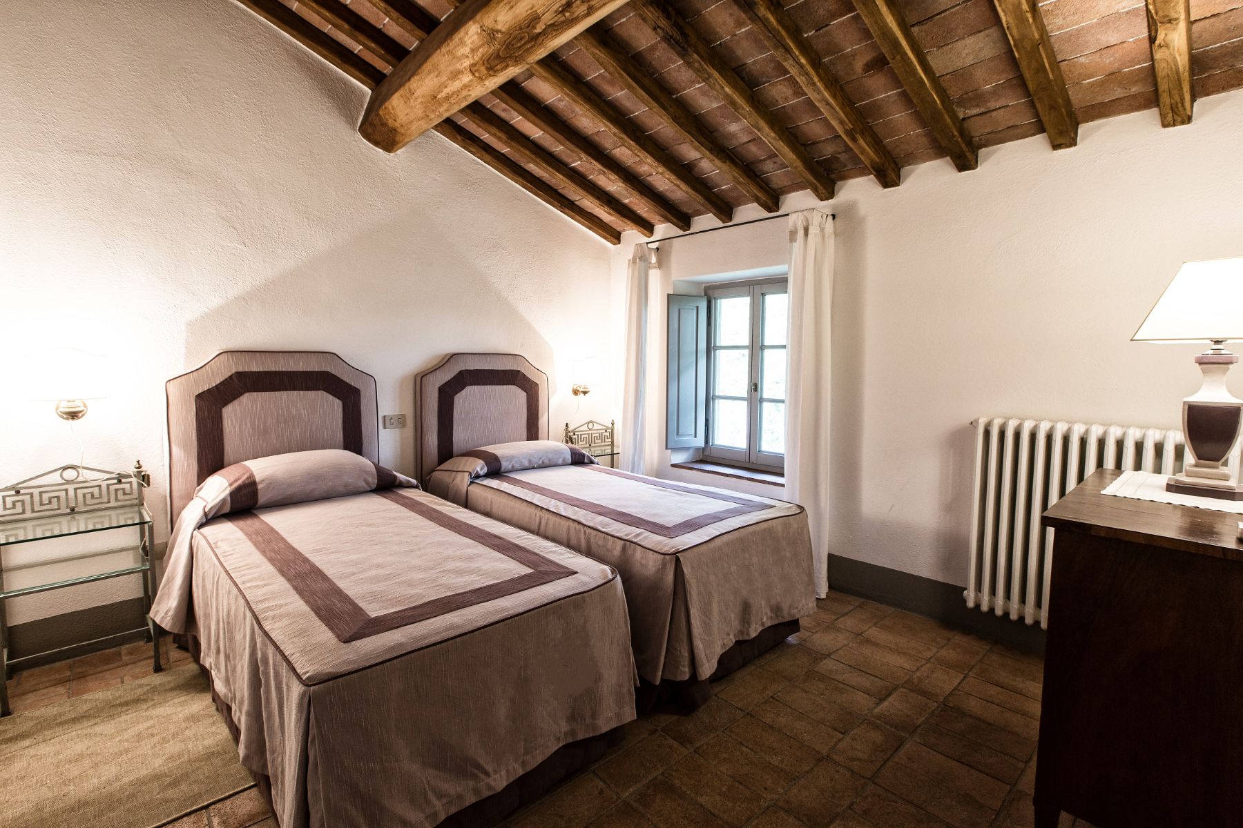 Twin room with purple bedding and wooden beams and a small window at the side at Il Prato di Vignamaggio in Tuscany