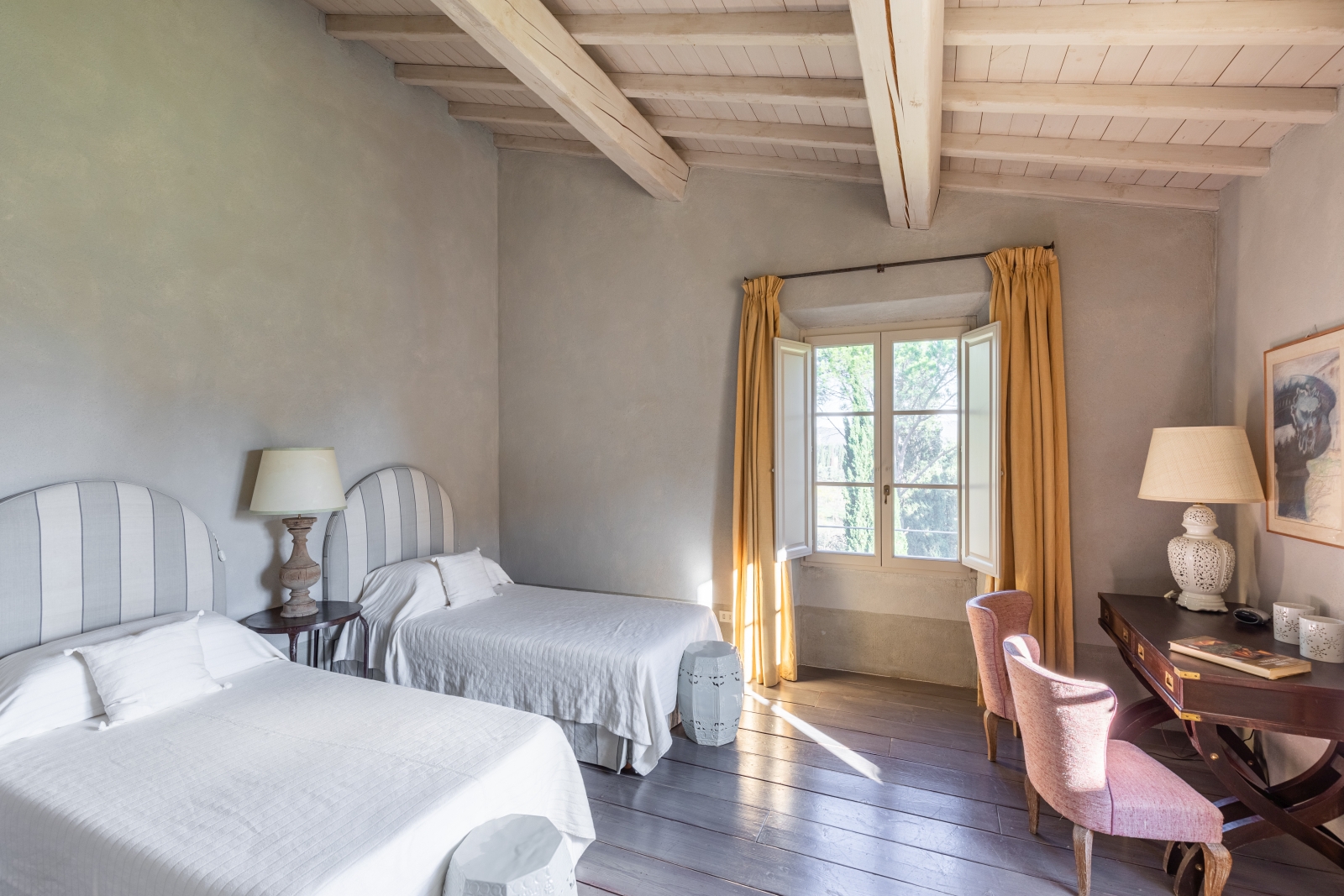 Bedroom with twin beds, bedside table, lamps, desk, chairs and large window at Il Serratone in Tuscany, Italy