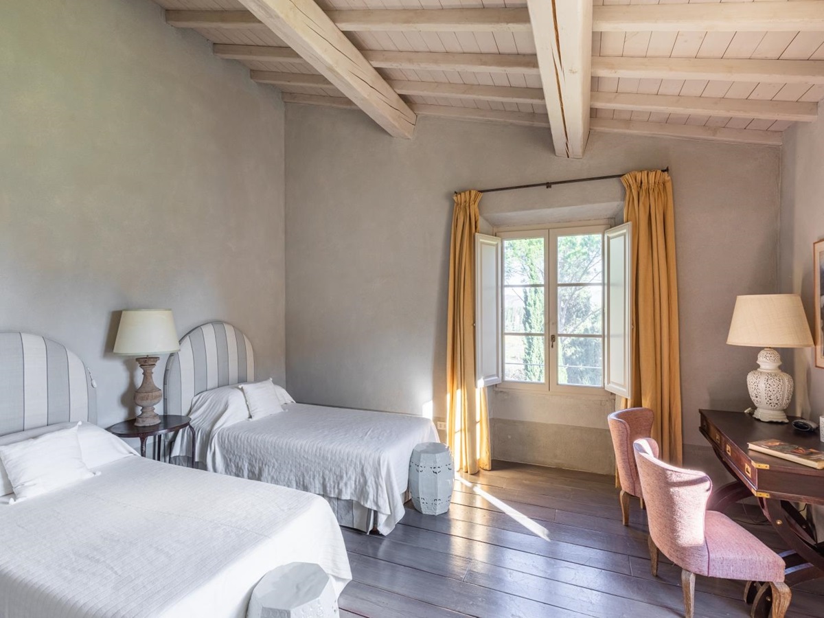 Bedroom with twin beds, bedside table, lamps, desk, chairs and large window at Il Serratone in Tuscany, Italy