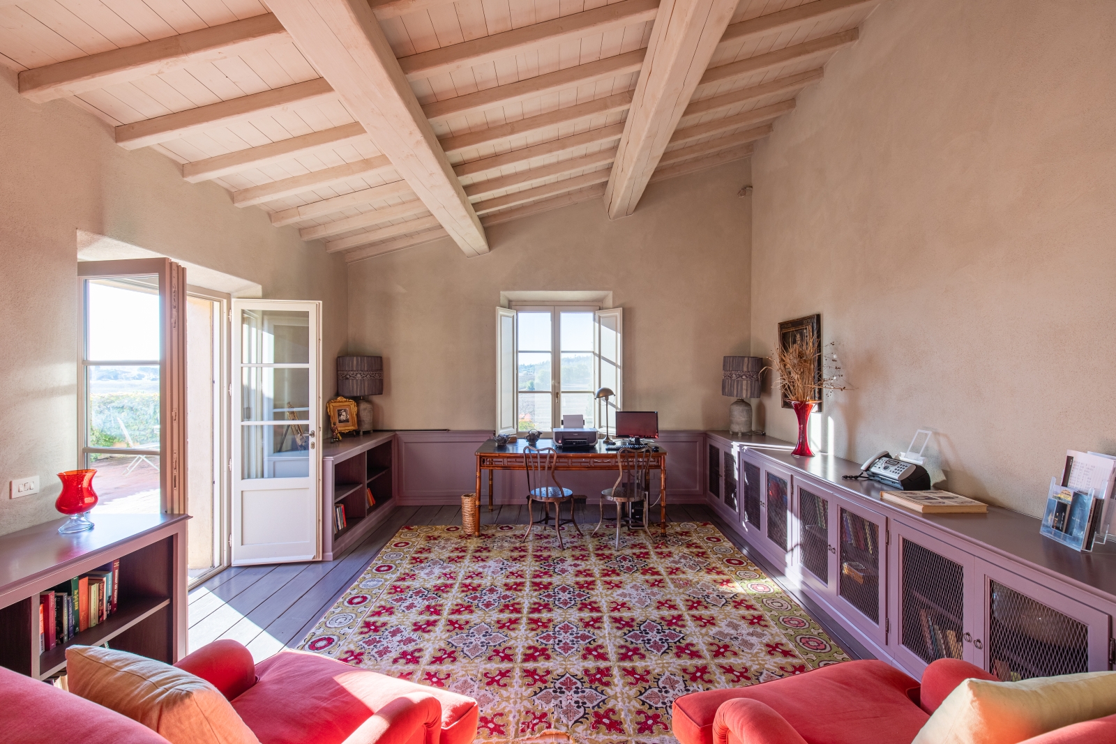 Study with armchairs, bookshelves, desk, chairs, lamps and French doors at Il Serratone in Tuscany, Italy