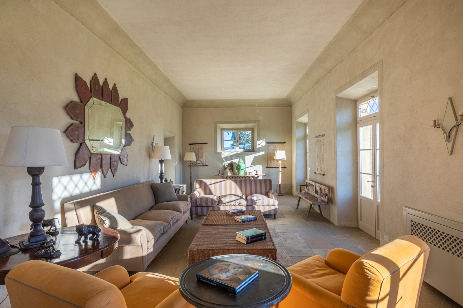 Living room with armchairs, sofas, coffee tables, lamps, mirror and French doors at Il Serratone in Tuscany, Italy