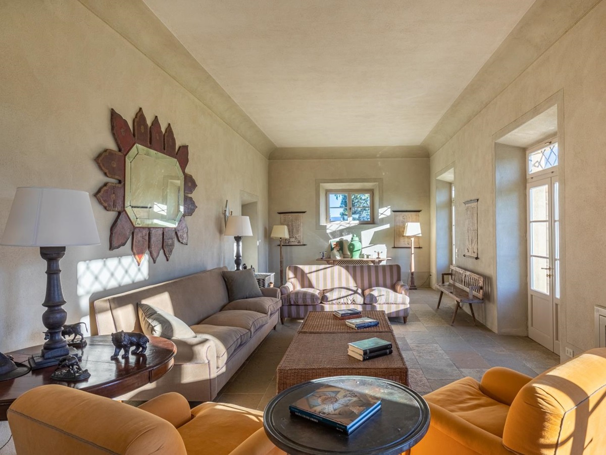 Living room with armchairs, sofas, coffee tables, lamps, mirror and French doors at Il Serratone in Tuscany, Italy