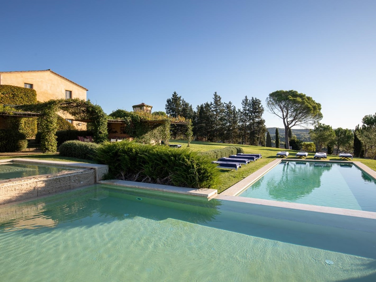 Large swimming pool in garden with sun loungers, grass, hedges & trees at Il Serratone in Tuscany, Italy