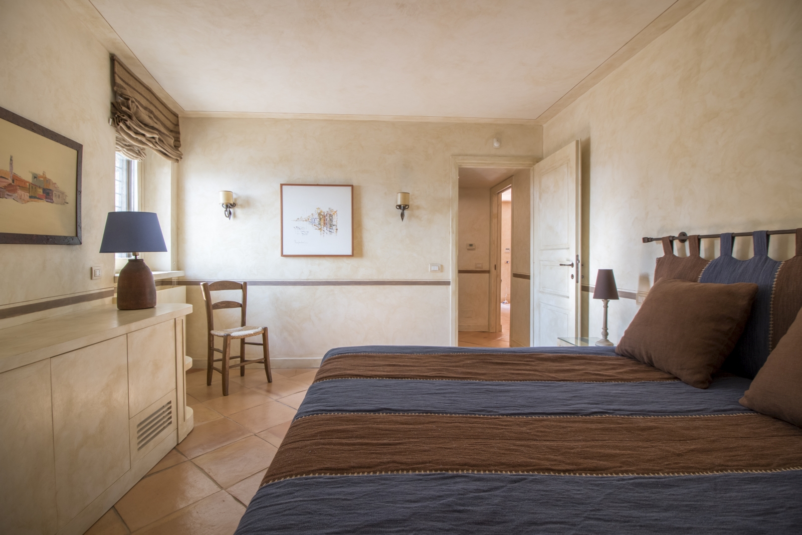 Bedroom with double bed, bedside table, lamp, cupboards, picture frames and chair at La Feniglia in Porto Ercole in Tuscany