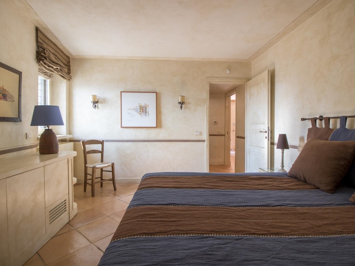 Bedroom with double bed, bedside table, lamp, cupboards, picture frames and chair at La Feniglia in Porto Ercole in Tuscany