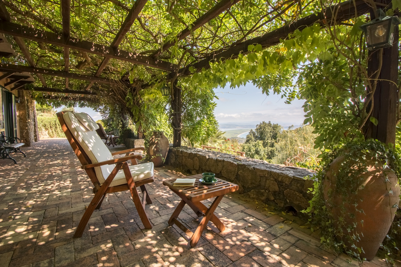 Terrace with chairs, coffee table, vines and sea view at La Feniglia in Porto Ercole in Tuscany