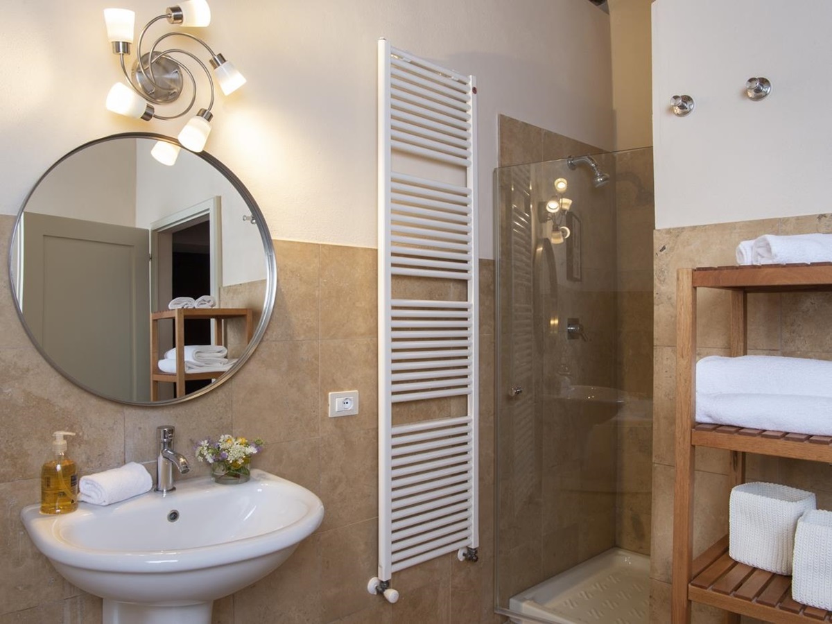 Bathroom with sink, mirror, towel rail, shelves and shower at La Gavelli in Tuscany, Italy