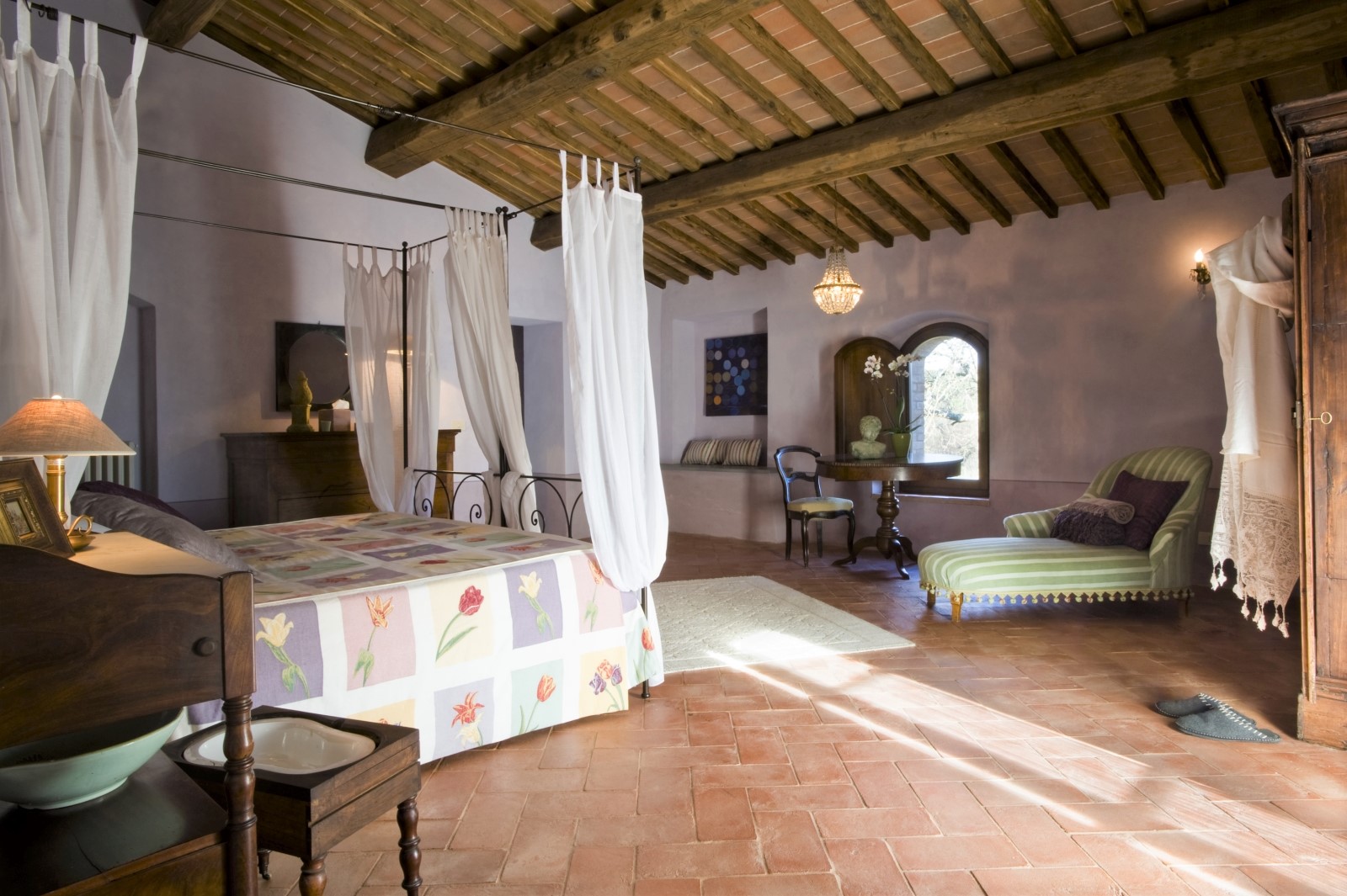 Bedroom with four poster double bed, chaise longue, table, chair and chandelier at La Gavelli in Tuscany, Italy