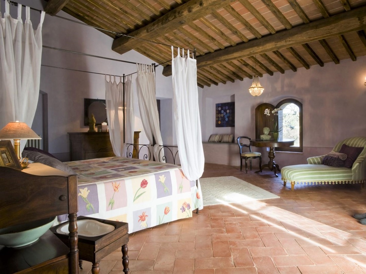 Bedroom with four poster double bed, chaise longue, table, chair and chandelier at La Gavelli in Tuscany, Italy